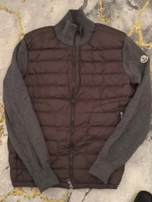 Grå jacka från Moncler - Snygg äkta teddyjacka från Moncler i mörkgrått med quiltad front och stickade ärmar. Jackan har hög krage, dragkedja framtill och Moncler-logga på ärmen. Perfekt för dig som vill ha en stilren och mysig jacka med exklusiv känsla.