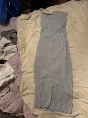 Ljusgrå lång klänning - En enkel och stilren ljusgrå lång klänning i mjukt stretchigt material. Klänningen har en rak passform och är ärmlös, vilket ger en avslappnad men ändå snygg look. Perfekt för dig som gillar minimalistisk stil.