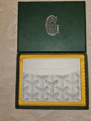 Vit Goy4rd plånbok - Snygg och exklusiv vit plånbok i skinn med det klassiska mönstret och flera kortfack. Perfekt för dig som vill ha något stilrent och lyxigt i fickan. Kommer i original ask.