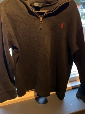 Svart halvzip från Polo Ralph Lauren - Svart långärmad tröja från Polo Ralph Lauren med halv dragkedja och klassisk röd broderad logga på bröstet. Tillverkad i 100% bomull.