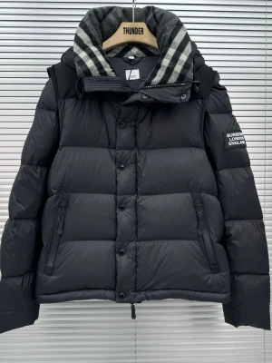 Svart pufferjacka från Burberry - Säljer en svart pufferjacka från Burberry med avtagbara ärmar så den kan bäras som väst. Jackan har en stor krage med grått och vitt rutmönster, dragkedja och knappar framtill samt två fickor med dragkedja. Märke på ärmen och riktigt schysst oversized look.