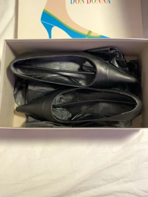 Svarta pumps från Don Donna - Klassiska svarta pumps från Don Donna med spetsig tå och låg klack. Skorna är tillverkade i slätt skinn och har en elegant och tidlös design som passar till många olika outfits.