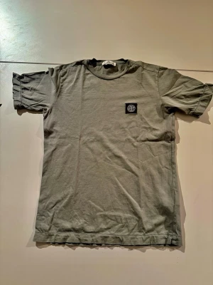 Grön t-shirt från Stone Island - Säljer en stilren grön t-shirt från Stone Island med klassisk rund hals och korta ärmar. T-shirten har en liten svart patch med logga på bröstet och är gjord i mjuk bomull. Perfekt till vardags för en clean look.