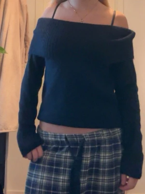 Mörkblå off shoulder stickad tröja - Snygg mörkblå stickad tröja med off shoulder-design och bred ribbad kant upptill. Tröjan har långa ärmar och en mjuk, mysig känsla. Perfekt för dig som vill ha en trendig och bekväm look till vardags.
