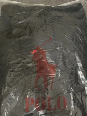 Svart dunjacka från Polo Ralph Lauren - Svart dunjacka från Polo Ralph Lauren med klassisk röd logga på bröstet. Jackan har huva, dragkedja framtill och två sidofickor med dragkedja. Perfekt för kalla dagar och riktigt snygg streetstil.