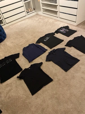 Svarta och mörkblå t-shirts från Nike, Boss & NY - Säljer ett paket med sju t-shirts i svart och mörkblått från märken som Nike, Boss och NY. Alla har klassisk passform och korta ärmar, vissa med tryck och loggor på bröstet. Perfekta basplagg för en clean och sportig stil.