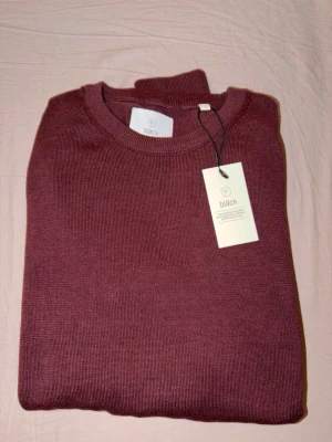 Vinröd stickad tröja från Bläck - Snygg vinröd stickad tröja från Bläck med rund halsringning och ribbade muddar. Tröjan har en minimalistisk design och är tillverkad i mjukt material som passar perfekt till lager på lager. Skandinavisk stil med fokus på detaljer.