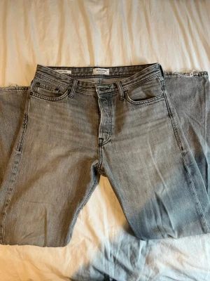 Grå jeans från Jack & Jones - Snygga grå jeans från Jack & Jones med klassisk femficksdesign och raka ben. Jeansen har en ljus tvätt och är tillverkade i bomullsmaterial för en skön känsla. Modellen är loose/chris. Perfekta för dig som gillar en enkel och clean stil. Strl W 29 L 32