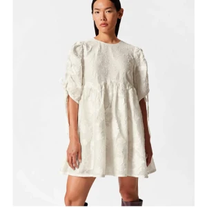 Vit kort klänning med broderi - Superfin vit kortklänning med broderade detaljer och puffärmar. Klänningen har en lös passform och är tillverkad i ett lätt material som passar perfekt till varmare dagar. Söt och trendig modell med rund halsringning och knytband vid ärmarna.  Perfekt klänning för student eller midsommar!