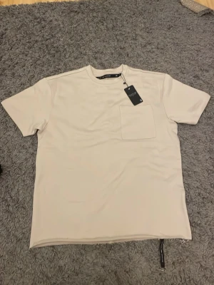 Beige t-shirt från lager 157 - Beige t-shirt från lager 157 med en bröstficka.    T-shirten har en bra passform och är tillverkad i mjuk bomull, perfekt för en clean och stilren look.