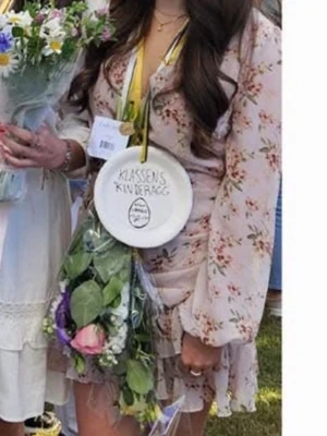 Ljusrosa blommig omlottklänning - Supersöt ljusrosa omlottklänning från Nly trend med blommigt mönster. Klänningen har volangdetaljer, v-ringning och långa ärmar i ett tunt, luftigt material. Perfekt för sommarens alla tillfällen! Ena sömmen på ärmen har gått upp och skulle behövas dra åt på något sätt