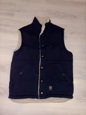 Vändbar väst från Jack & Jones - Snygg och praktisk vändbar väst från Jack & Jones. Ena sidan är marinblå och den andra i  teddy så den passar bra för att variera stil efter outfit. Den är för liten för mig så den har aldrig använts. Hör av dig vid frågor 😄