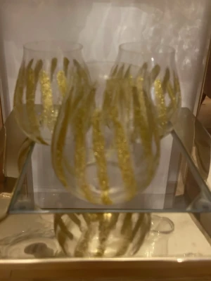 Glittrig guldig randig glas - Säljer en unik väst med glittriga, guldiga ränder som verkligen sticker ut. Västen har en klassisk passform och är perfekt för dig som vill ha något extra. Materialet är syntet och designen är riktigt trendig med sitt glittriga mönster.