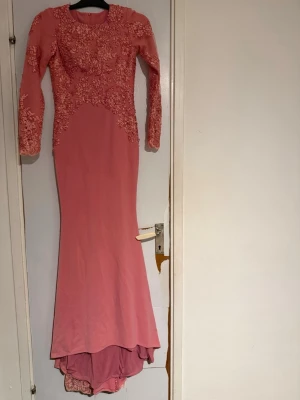 Rosa långklänning med spetsdetaljer - Supersnygg rosa långklänning med långa ärmar och broderade spetsdetaljer över hela överdelen och ärmarna. Klänningen har en figurnära passform och rund halsringning. Perfekt för bal eller festliga tillfällen! Den är självsydd