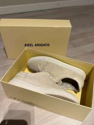 Beige mocka sneakers från Axel Arigato Clean 90 - Stilrena sneakers från Axel Arigato i beige mocka med vit sula. Klassisk låg modell med snörning och minimalistisk design. Perfekta för dig som gillar en clean och modern look. Använda ett fåtal gånger. Skorna är defektfria. Lådan medföljer! 