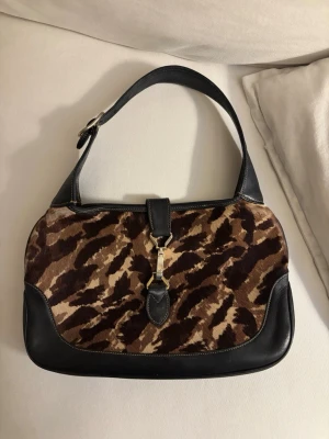 Gucci Jackie väska - Vintage Gucci Jackie väska i skinn och pony hair. Kommer med en förlängsningsrem. Liten fläck på insidan av väskan, finns tecken på användning men den är i bra skick.