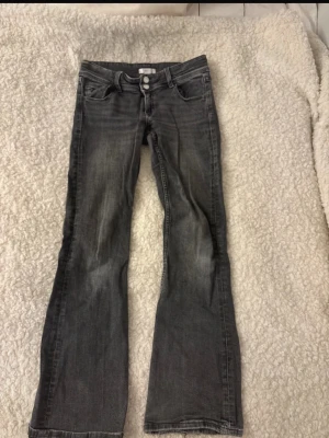 Grå bootcut jeans från Gina Tricot - Snygga grå bootcut jeans från Gina Tricot med två knappar i midjan och klassisk femficksmodell. Jeansen har en lätt tvättad look och raka ben som går ut något nedtill. Perfekta för en avslappnad och trendig stil. Storlek 152