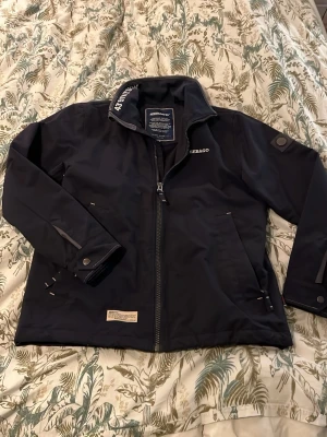 Svart/marinblå jacka från Sebago, M - Säljer en svart skepparjacka från Sebago i storlek M. Jackan har hög krage med tryck, dragkedja framtill, två sidofickor (med och utan dragkedja) och detaljer med tryckknappar vid ärmsluten. Materialet är slitstark nylon med fleecefodran för värme och jackan har en clean, sportig look.