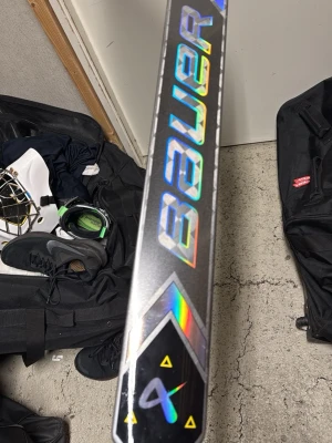 Bauer hockeyklubba shadow  - Säljer en hockeyklubba från Bauer i silver med holografiska och gula detaljer. Klubban har en modern design med geometriska mönster och tydlig Bauer-logga. Perfekt för dig som vill ha en snygg och lätt klubba till hockeyträningen. Intermediate 24”