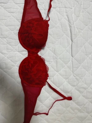 Röd spets-bh 75B - Snygg röd bh med vadderade kupor och blommigt spetsmönster. Axelbanden är justerbara och tyget är mjukt och följsamt. Perfekt för dig som vill ha något extra fint under kläderna. 75B men lite mindre.