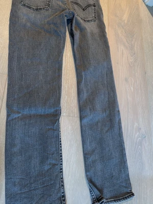 Grå Levi's 501 raka jeans - Säljer ett par klassiska grå Levi's 501 jeans med raka ben och fem fickor. Jeansen har knappgylf och är tillverkade i slitstark bomullsdenim. Perfekta för en avslappnad och tidlös stil.