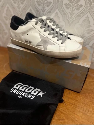 Golden Goose vita sneakers med stjärna - Tar byten mot loubs om dom är fräscha Golden Goose sneakers i vitt skinn med grå mockastjärna på sidan, grå snörning och svart hälparti. Klassisk låg modell med rund tå och platt sula. Snygg streetstil och ikonisk design med GGDB-detaljer.