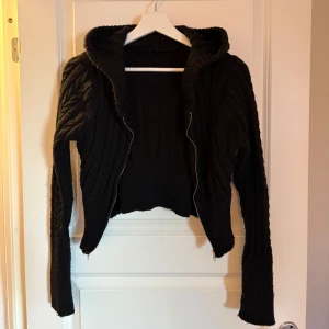 Svart stickad hoodie från SHEIN - Säljer en svart stickad hoodie från SHEIN med dragkedja framtill. Tröjan har kabelstickat mönster, ribbad midja och långa ärmar. Perfekt för dig som gillar en avslappnad men ändå trendig stil. Passar till jeans eller kjol.