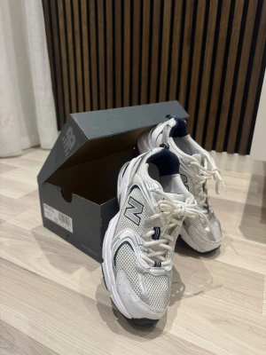 Vita New Balance 530 - Säljer ett par fräscha New Balance sneakers i vitt och silver med svarta och blå detaljer. Dem är i nyskick, mycket slitrena och fräscha. Nypris ligger runt 1500kr, säljer för endast 850kr.
