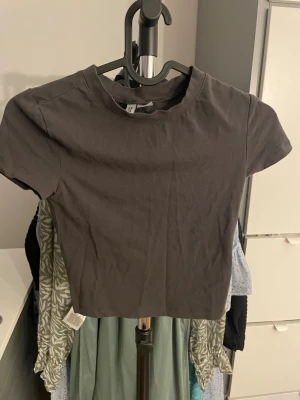 Mörkgrå croppad topp - Säljer en enkel och stilren mörkgrå croppad topp. Toppen har rund halsringning och korta ärmar, perfekt för att matcha med höga jeans eller kjol. Materialet är mjuk bomull som känns skönt mot huden.