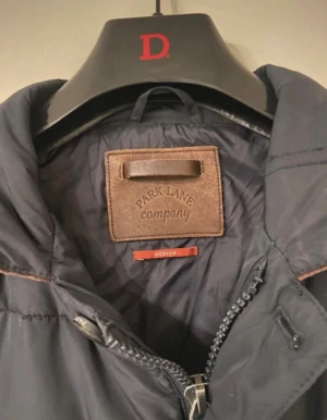 Mörkblå quiltad jacka från Park Lane - Snygg mörkblå quiltad jacka från Park Lane med bruna manchesterdetaljer på kragen. Jackan har knäppning med stora knappar, två rejäla fickor framtill och en klassisk, stilren look. Perfekt för dig som gillar tidlös design.