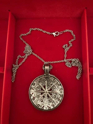 Silvrigt halsband med rund medaljong - Unikt silvrigt halsband med rund medaljong. Ena sidan har ett detaljerat blommönster med små cirklar och ornament, andra sidan har ett stjärnliknande mönster med prickar och linjer. Kedjan är tunn och har ett klassiskt lås. Perfekt för dig som gillar boho eller vintage vibes.