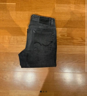 Grå jeans från Jack & Jones, storlek 152 - Snygga grå jeans från Jack & Jones i klassisk femficksmodell. Jeansen har en rak passform och normal midja, med slitningar som ger en cool, lite tvättad look. Perfekta för dig som gillar stilrena och bekväma jeans med en modern vibe.