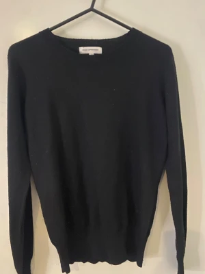 Svart stickad tröja Moss Copenhagen - En stilren svart stickad tröja från Moss Copenhagen med rund hals och långärmad passform. Perfekt för dig som gillar enkel och klassisk look. Materialet är mjukt och skönt, och tröjan har en normal passning som funkar till många outfits.