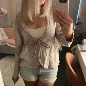 Beige mönstrad kofta från Happy Holly - Supersöt beige kofta från Happy Holly med diskret mönster i vitt. Koftan har knytband framtill och en lätt figursydd passform. Långärmad och i mjukt stickat material, perfekt att slänga över ett linne eller t-shirt. Koftan är i storlek 40/42 men funkar bra på mej som oftast har 38. 