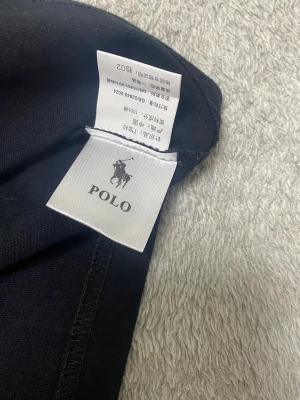 Svart t-shirt från Polo Ralph Lauren - Svart t-shirt från Polo Ralph Lauren med klassisk rund hals och korta ärmar. T-shirten är i mjuk bomull och har den ikoniska röda broderade Polo-loggan på bröstet. Perfekt basic med snygg passform och stilren look.    Slim fit 