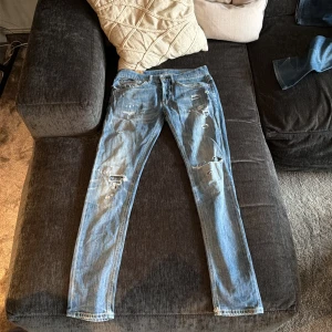 Dondup ljusblå skinny jeans, strl 32 - Säljer ett par ljusblå skinny jeans från dondup i storlek 32. Jeansen har slitna detaljer och trasiga partier framtill för en cool, edgy look. Klassisk femficksmodell med metall-D på bakfickan och orange sömmar. Passar dig som gillar streetstyle.