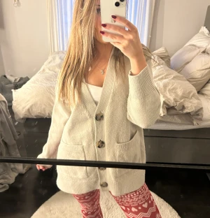 Beige stickad kofta med stora knappar - Mysig beige stickad kofta med två stora bruna knappar framtill och praktiska fickor. Koftan har lång ärm och en loose passform som ger en chill vibe. Perfekt att slänga på sig över ett linne eller t-shirt. Enkel och stilren design som funkar till många outfits.