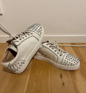 Vita Louboutin med spikar fram o bak - Säljer ett par sjukt snygga vita sneakers från Christian Louboutin med silverfärgade nitar på tå och häl. Mycket bra skick, men ska tvätta innan frakt. Storlek 42, passar även 43. Köpta här hemma p plick så är osäker på äkthet, därav pris. Box och dustbag medföljer.