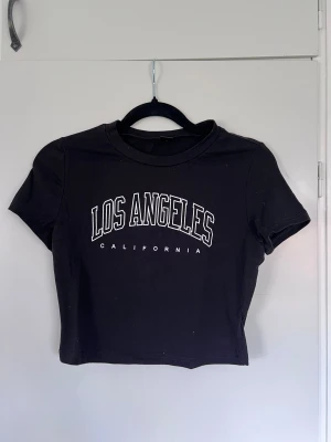 Svart croppad topp - Svart croppad topp med vit text. Rund halsringning och korta ärmar. T-shirten har en tightare passform och är gjord i mjuk bomull 💕 Passar bra på mig som normalt har S/M. Köper du innan kl 16:00 kan jag posta samma dag!