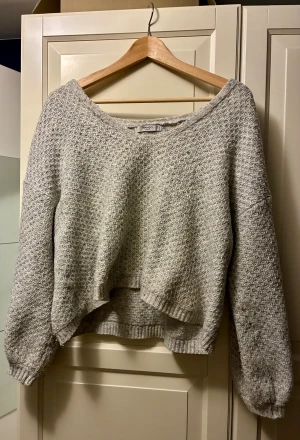 Grå stickad tröja från Mango - Mysig grå stickad tröja från Mango med grov struktur och avslappnad passform. Tröjan har lång ärm, bred halsringning och är något croppad framtill. Passar bäst till jeans eller kjol!