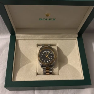 Apple Watch  -  herrklocka med svart urtavla, datumvisning och dagvisning. Boetten är i silverfärgat stål med räfflad guldfärgad bezel. Länken är tvåtonad i silver och guld. Kommer i original grön -box med certifikat och påse.