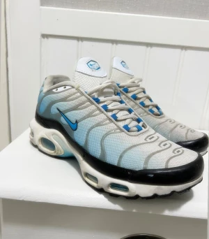 Nike sneakers blå/vit strl 41 - Nike sneakers i storlek 41 med mesh-ovandel i vitt och ljusblått, svarta detaljer och blå swoosh. Skorna har tydliga vågformade linjer, snörning med blå öglor och en kraftig sula med synliga luftbubblor. Perfekta för dig som gillar sportig och modern stil. Använd 3/4 gånger, eftersom vill köpa ett par vita Nike sneakers. 