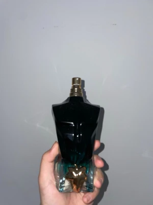 Jean Paul Gaultier Le Male parfym - Unik parfymflaska formad som en manlig torso i mörkblått glas med gulddetaljer. Flaskan har en elegant och konstnärlig design som verkligen sticker ut på hyllan. Perfekt för dig som gillar ikoniska och stilrena dofter.