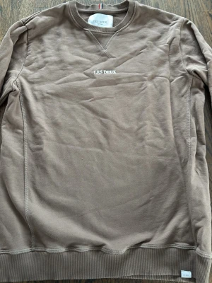 Brun sweatshirt från Les Deux - Snygg brun sweatshirt från Les Deux med broderad logga på bröstet. Tröjan har rund halsringning, ribbade muddar och är tillverkad i mjuk bomull. Perfekt för en avslappnad och stilren look.