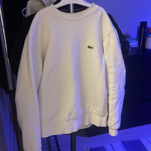Vit sweatshirt från Lacoste - Säljer en stilren vit sweatshirt från Lacoste i klassisk passform. Då jag inte använder tröjan längre och något stort på mig, använd ungefär 10 gånger mer eller mindre