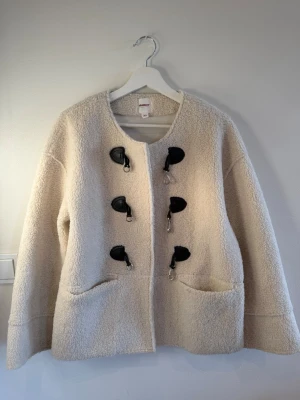 Krämvit teddyjacka från Dobber XS - Mysig krämvit teddyjacka från Dobber med rund halsringning och fyra svarta toggle-knäppen i läderimitation. Jackan har två stora fickor framtill och är tillverkad i fluffigt teddy-material som ger en cool och avslappnad look. Lite större i storleken så skulle sitta lika bra på S. Nypriset ligger på 1299kr men jackan är helt slutsåld. 💗