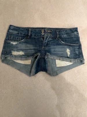 Blå slitna jeansshorts med rå kant - Snygga lågmidjade blå jeansshorts från Tally Weijl. Dom är i bra skick! Skriv för frågor och prisförslag. Midjemått: 38cm tvärs över, grenhöjd: 13cm