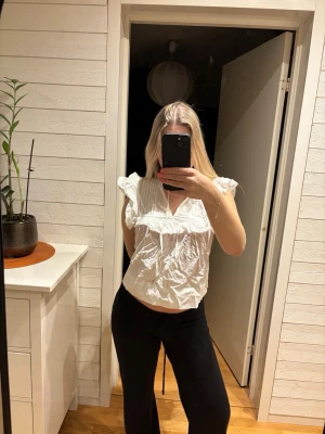 Vit volangblus med v-ringning - Säljer en söt vit blus med volangdetaljer och v-ringning. Blusen har korta ärmar med volanger. Fint sick! 