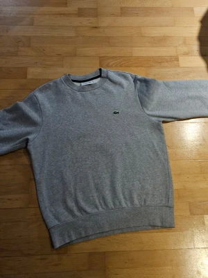 Grå sweatshirt från Lacoste - Lacoste grå crewneck – storlek M, mycket fint skick Säljer en stilren och tidlös Lacoste sweatshirt i grått med klassiska krokodilloggan på bröstet. En clean tröja som passar perfekt till både jeans och mer avslappnade outfits. Tröjan är i storlek M (Classic Fit) och är inte använd mycket alls, vilket märks på skicket – fräsch, mjuk och utan fläckar eller slitage. Perfekt för vardag, skola eller en snygg casual look. 