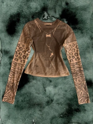 Grå långärmad topp med mönster - Cool långärmad topp från mitt märke Funkyfig i grå och vit med leopard- och zebramönster på ärmarna. Figurnära passform och unika detaljer framtill. Perfekt för dig som vill sticka ut med ett djurinspirerat plagg.